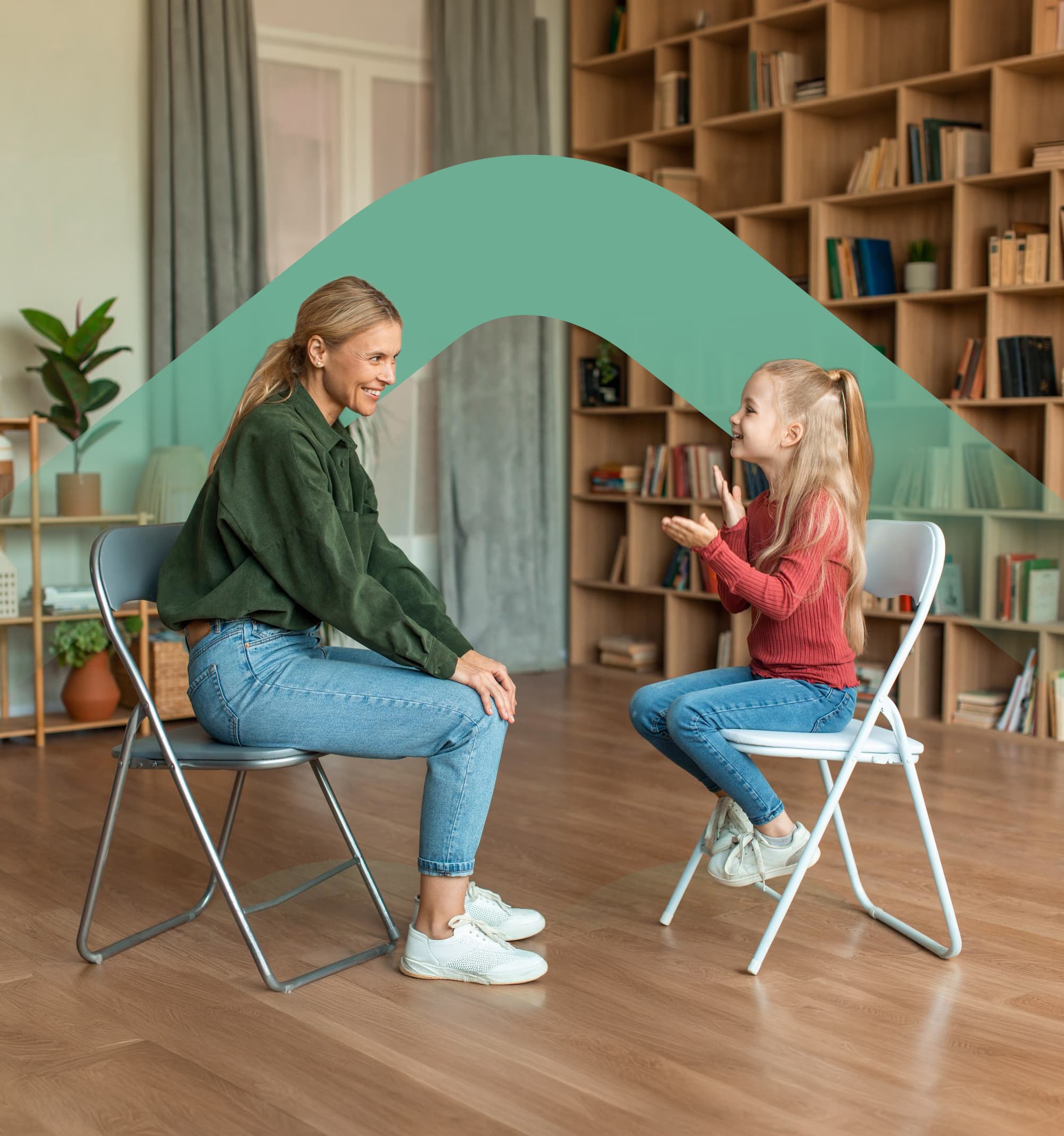 A therapist and a young girl sitting face to face on chairs, clapping along together