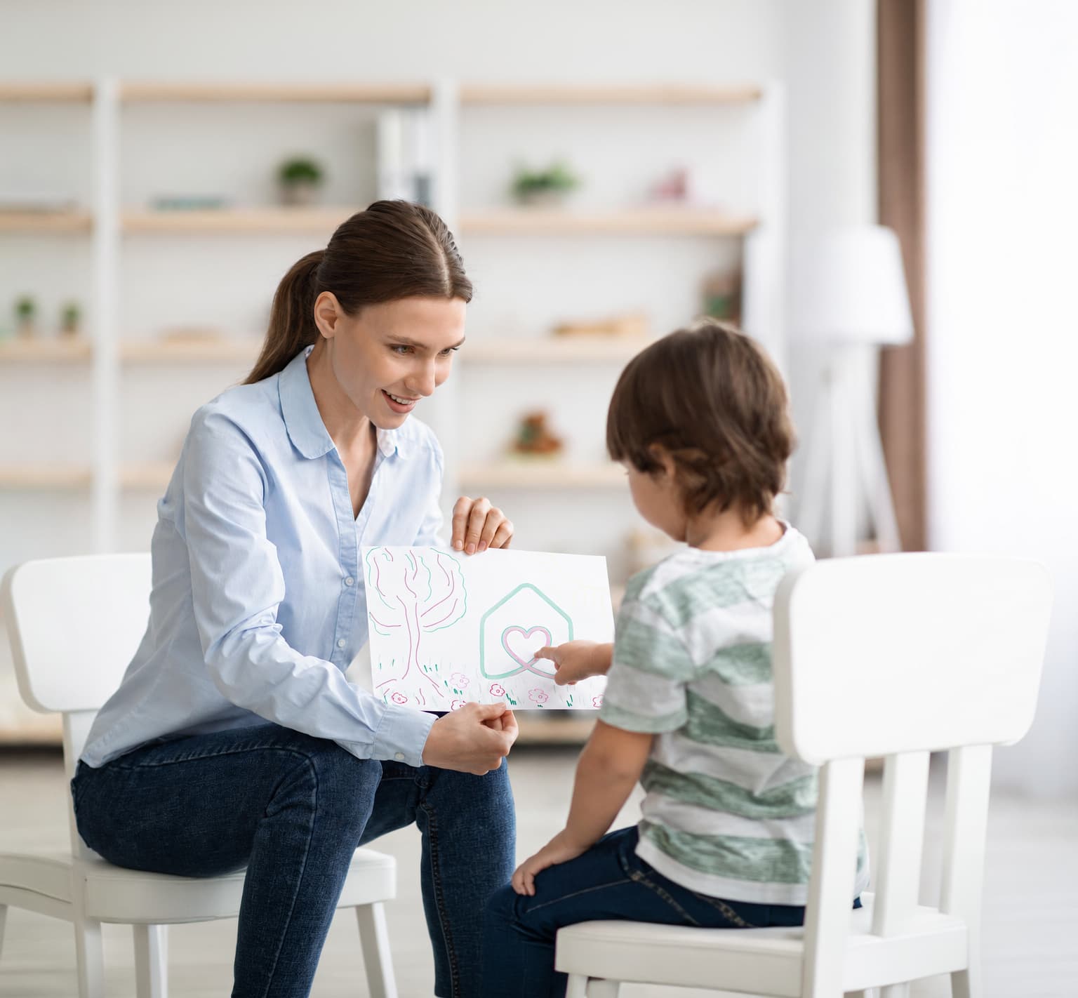 A therapist showing a young child a drawing of a house with a heart inside it